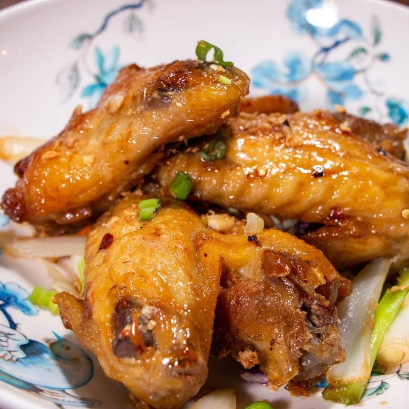 Golden brown chicken wings garnished with green onions and garlic, served on a decorative plate.
