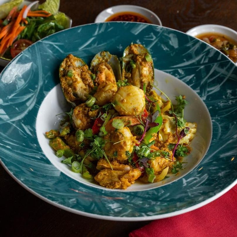 Seafood curry with mussels, shrimp, and scallops, garnished with herbs in a teal and white bowl.