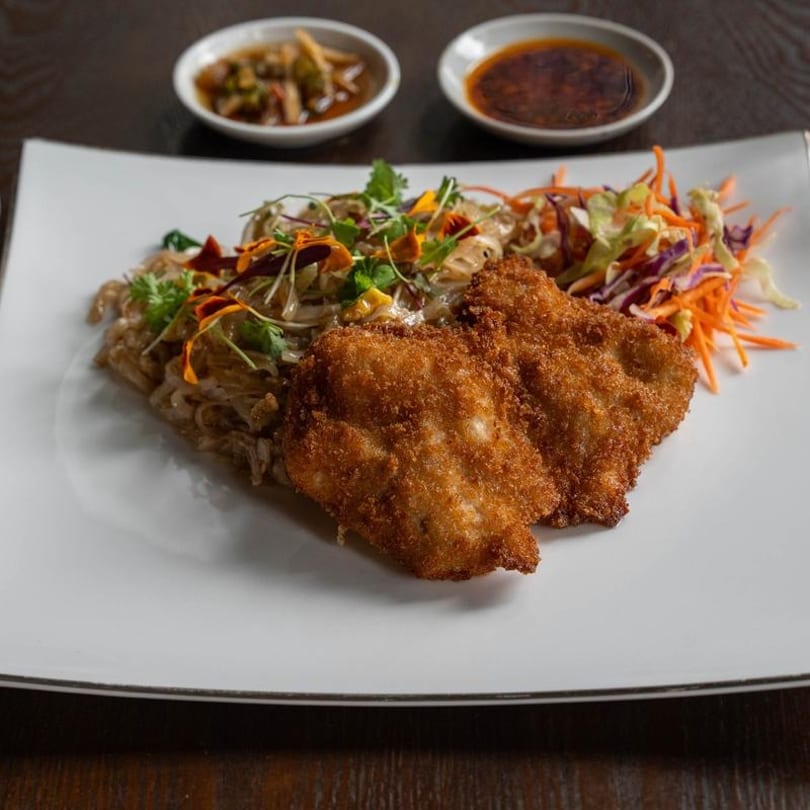 Crispy fried chicken with noodles, colorful vegetables, and two dipping sauces on a white plate.