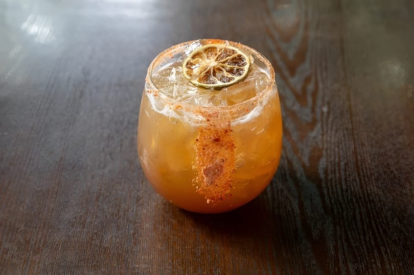 A spiced cocktail with a dried lime slice and ice, on a dark wooden table.