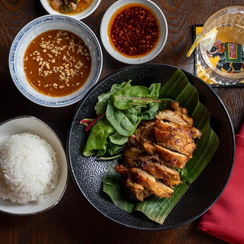 Grilled chicken with a side salad, rice, peanut sauce, chili oil, and a drink.