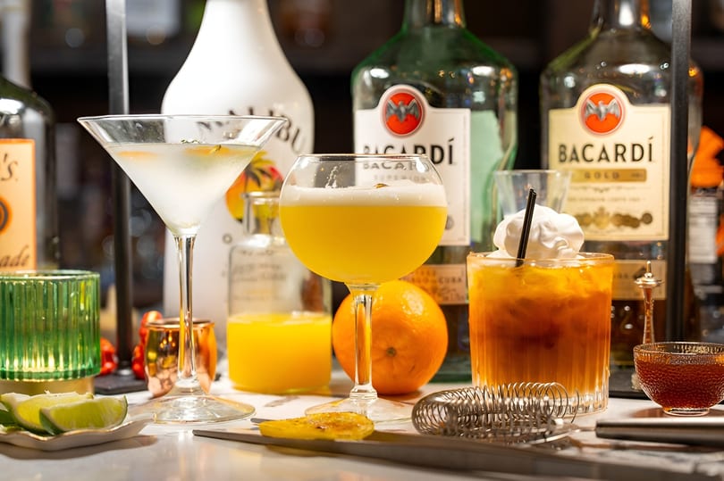 Three colorful cocktails, a martini, a yellow drink, and a brown drink with whipped cream, on a bar.